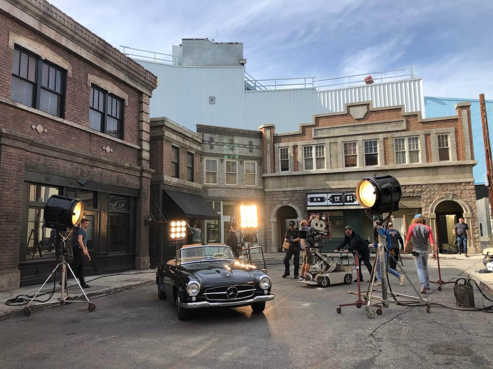 A film crew shoots a scene with a vintage car in a classic urban set.