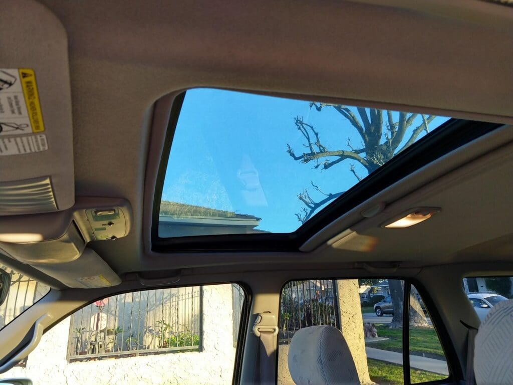 View through a car's sunroof showing clear blue sky and tree branches.
