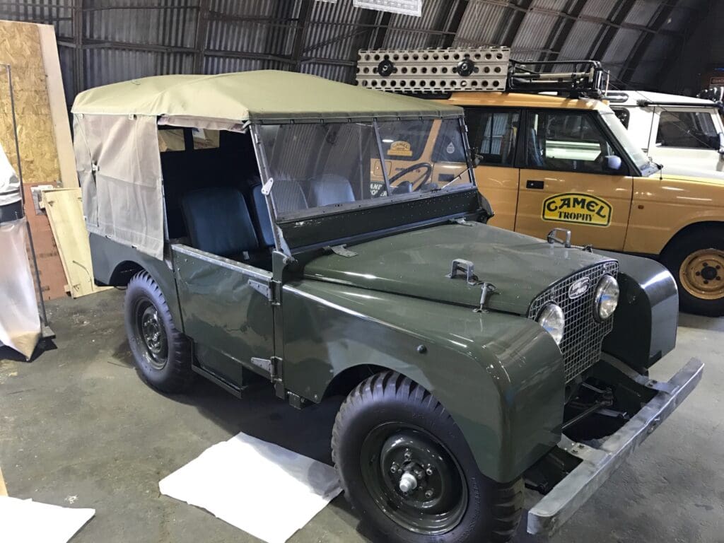 Vintage military jeep with canvas top in a warehouse setting.