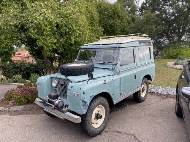 Vintage light blue Land Rover parked near trees.