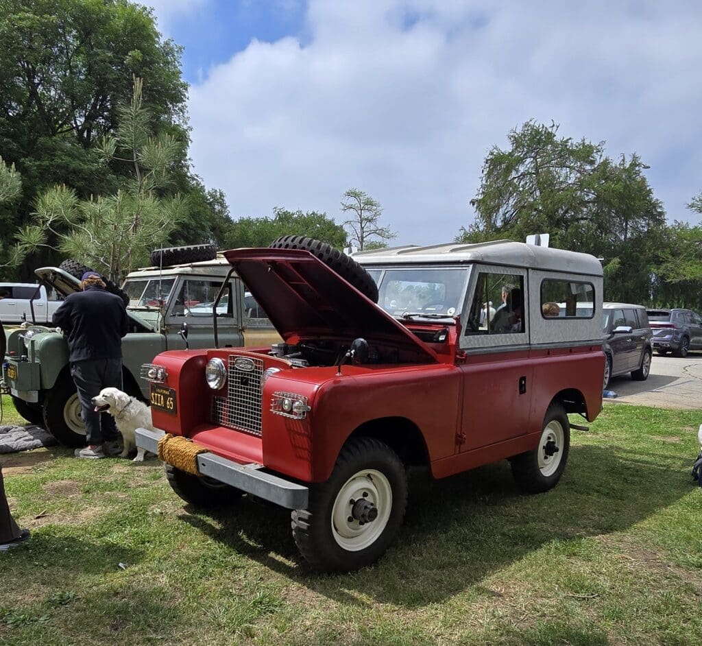 Classic red and white Land Rover with hood open at outdoor event.