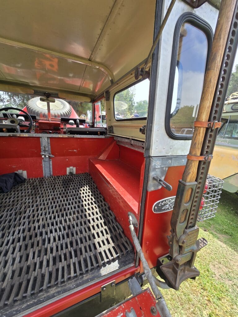 Classic red and white Land Rover with hood open at outdoor event.