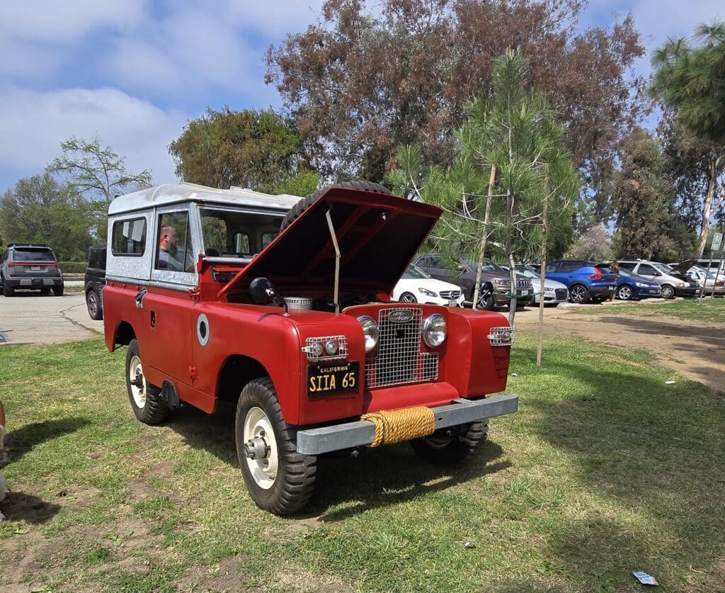 Classic red Land Rover with hood open at outdoor event.