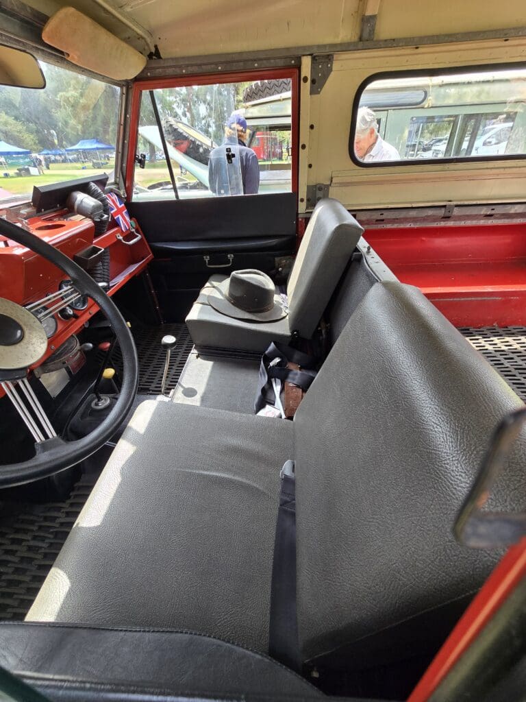 Interior of a vintage vehicle with gray bench seats and red accents.