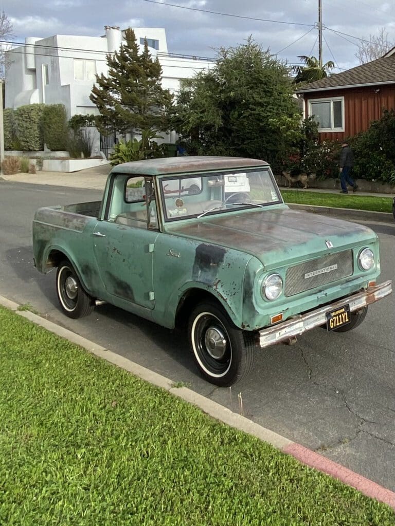 A vintage turquoise pickup truck parked on a suburban street.
