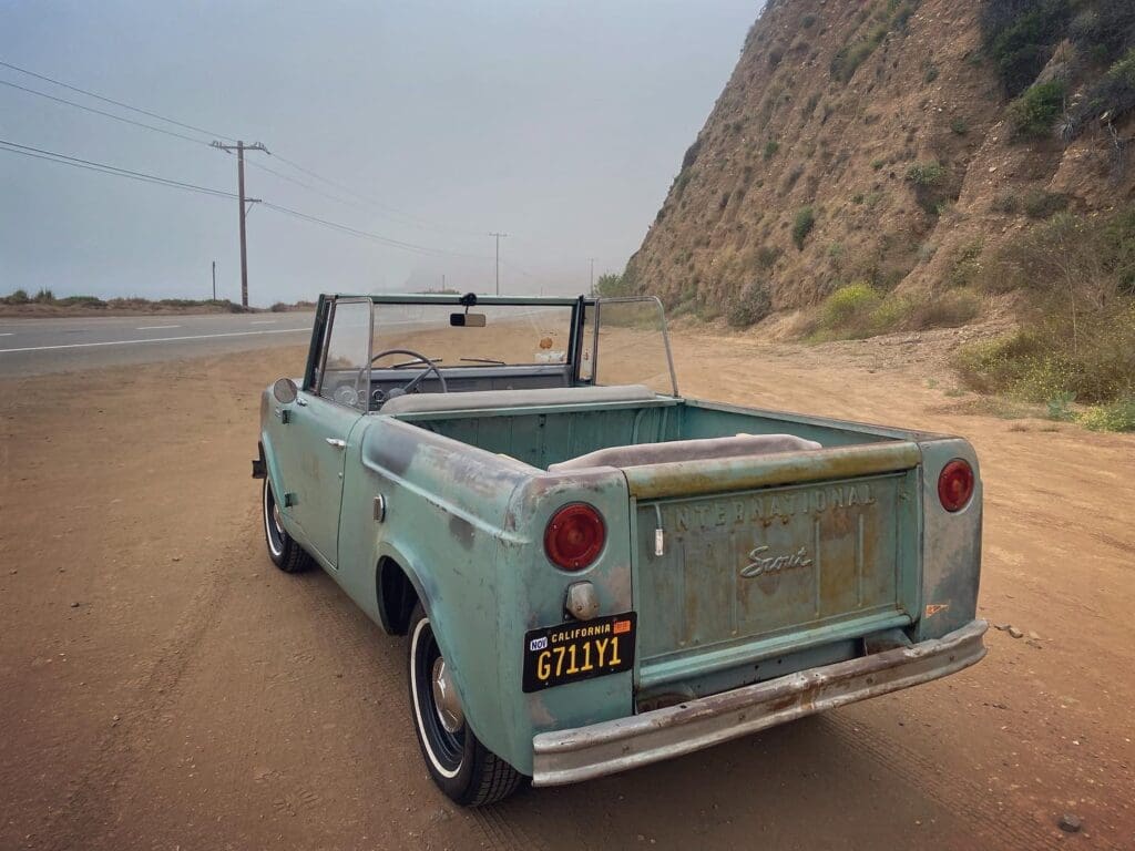 Vintage turquoise pickup truck parked near a rocky hillside.