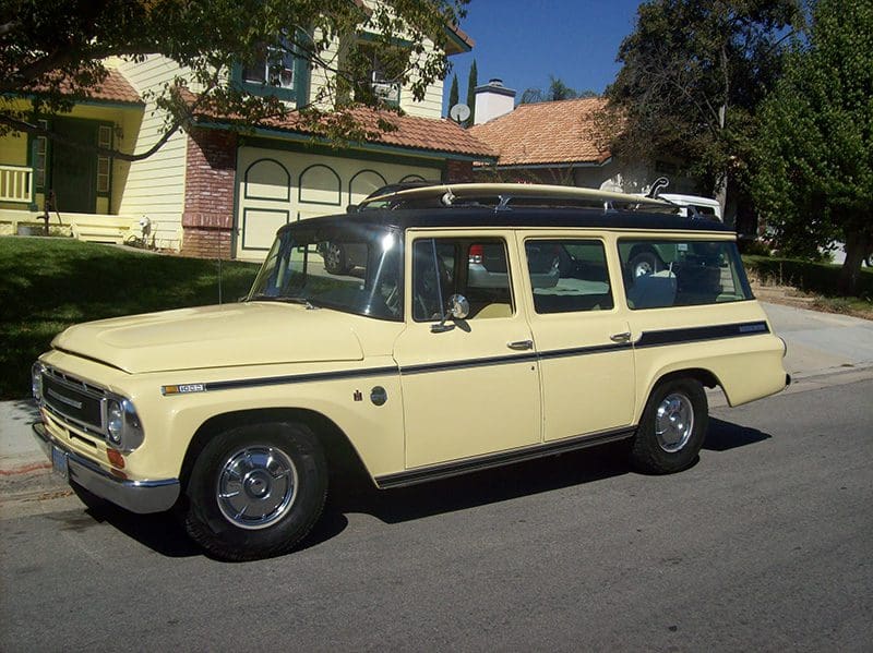 Vintage yellow station wagon parked on the street in front of houses.
