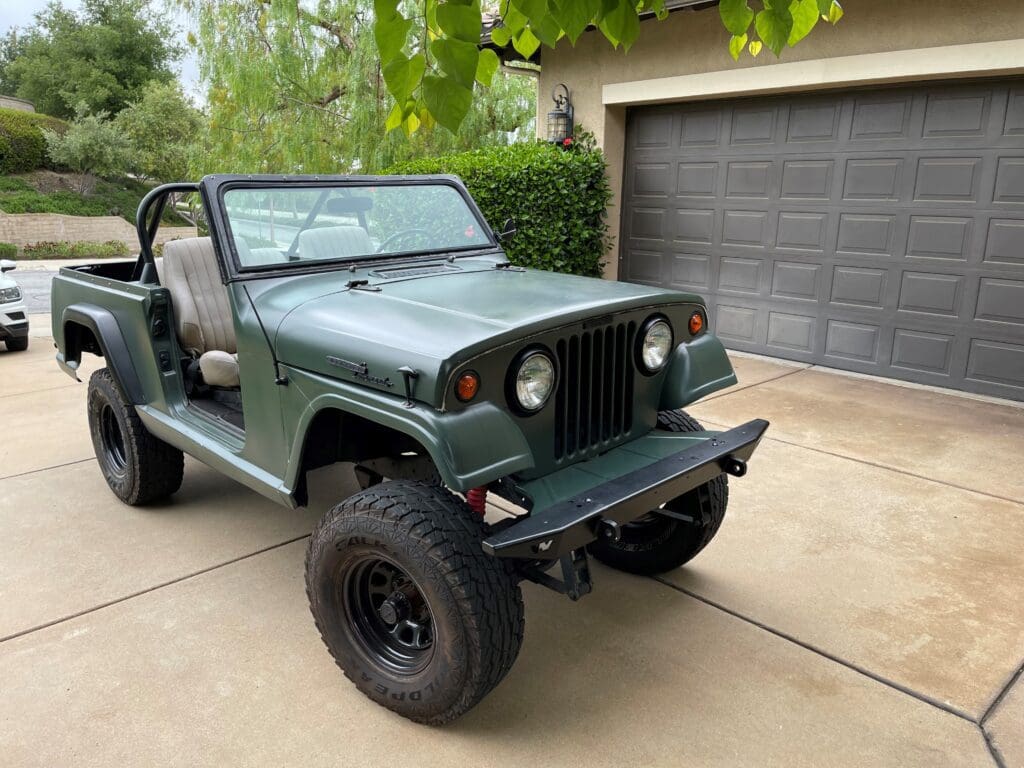 Classic green Jeep parked in a driveway with an open roof and rugged tires.