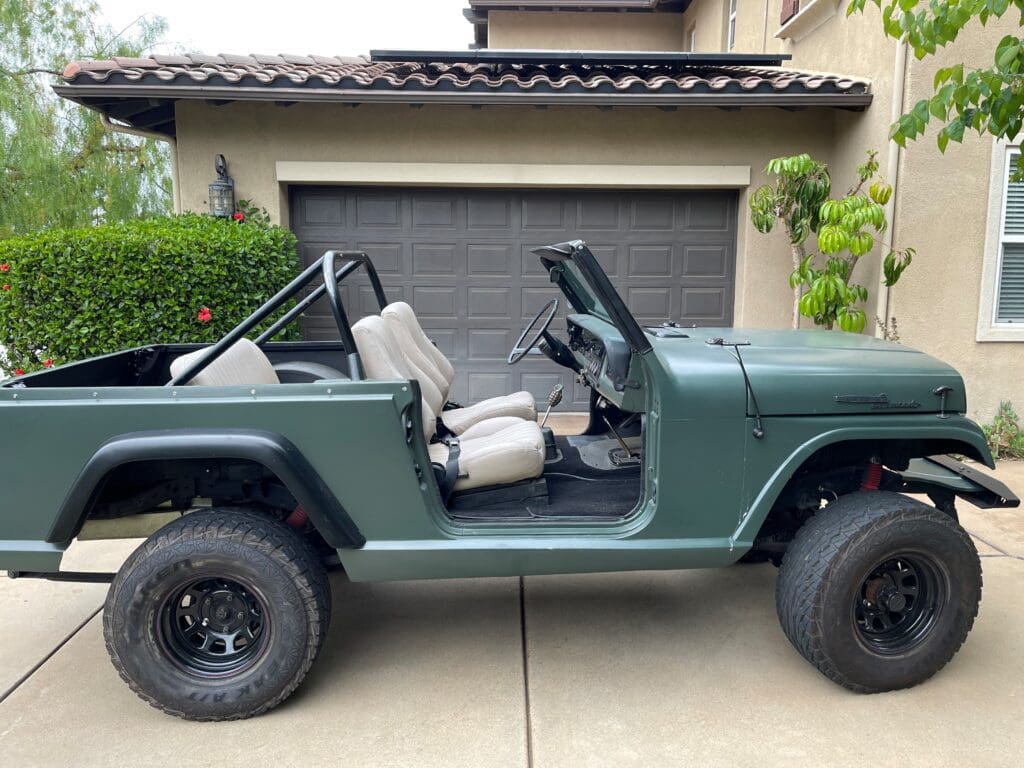Green open-top jeep parked in front of a garage.