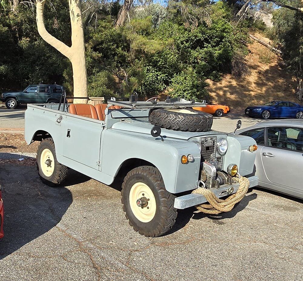 Classic light blue Land Rover parked outdoors with vintage gear on the hood.
