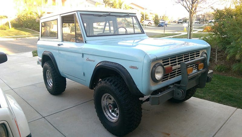 Light blue classic Ford Bronco parked outdoors with large tires.