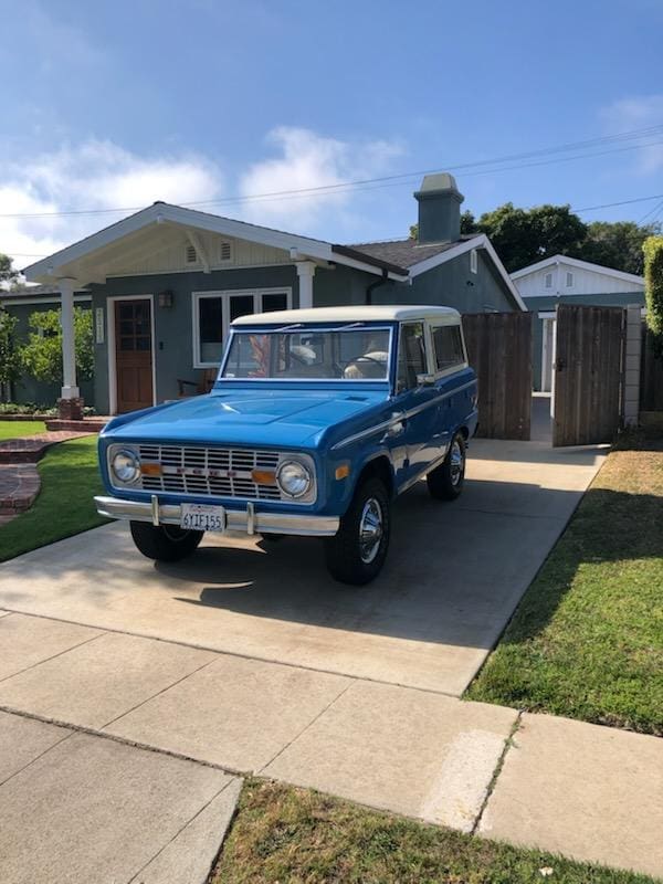 Classic blue Ford Bronco parked in a suburban driveway on a sunny day.