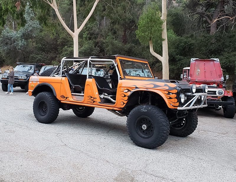 Orange off-road Jeep with no doors parked in a wooded area.