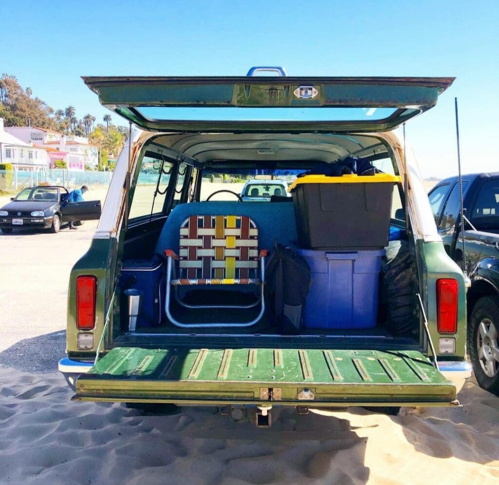 Open car trunk with colorful cushions and a patterned bag on a sunny day.