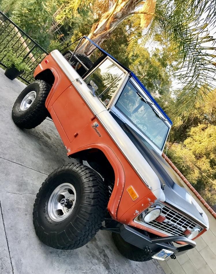 Classic orange lifted off-road truck parked outdoors.