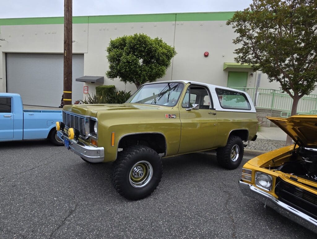 Classic yellow and white SUV parked outdoors near trees and a building.