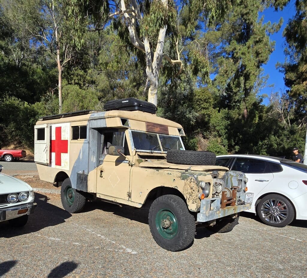 Vintage military ambulance parked outdoors under trees.