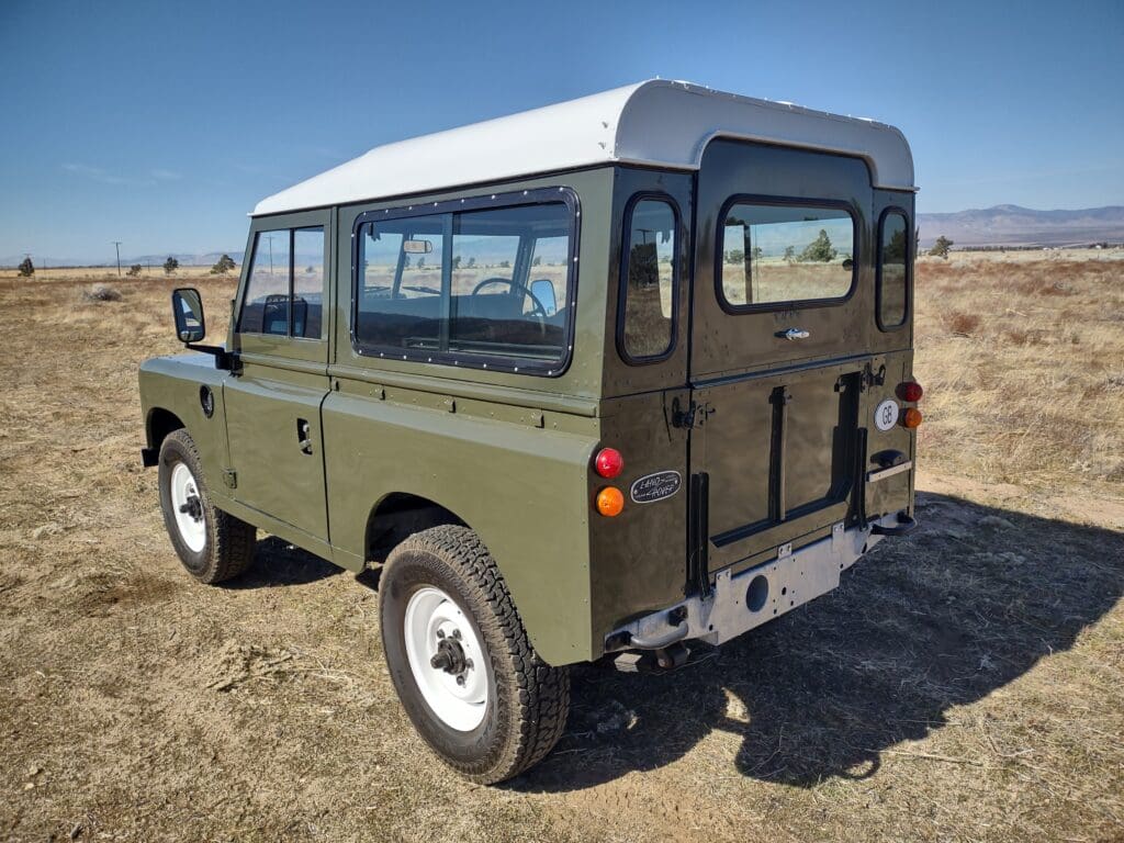 Classic green Land Rover parked on a sunny dirt road.