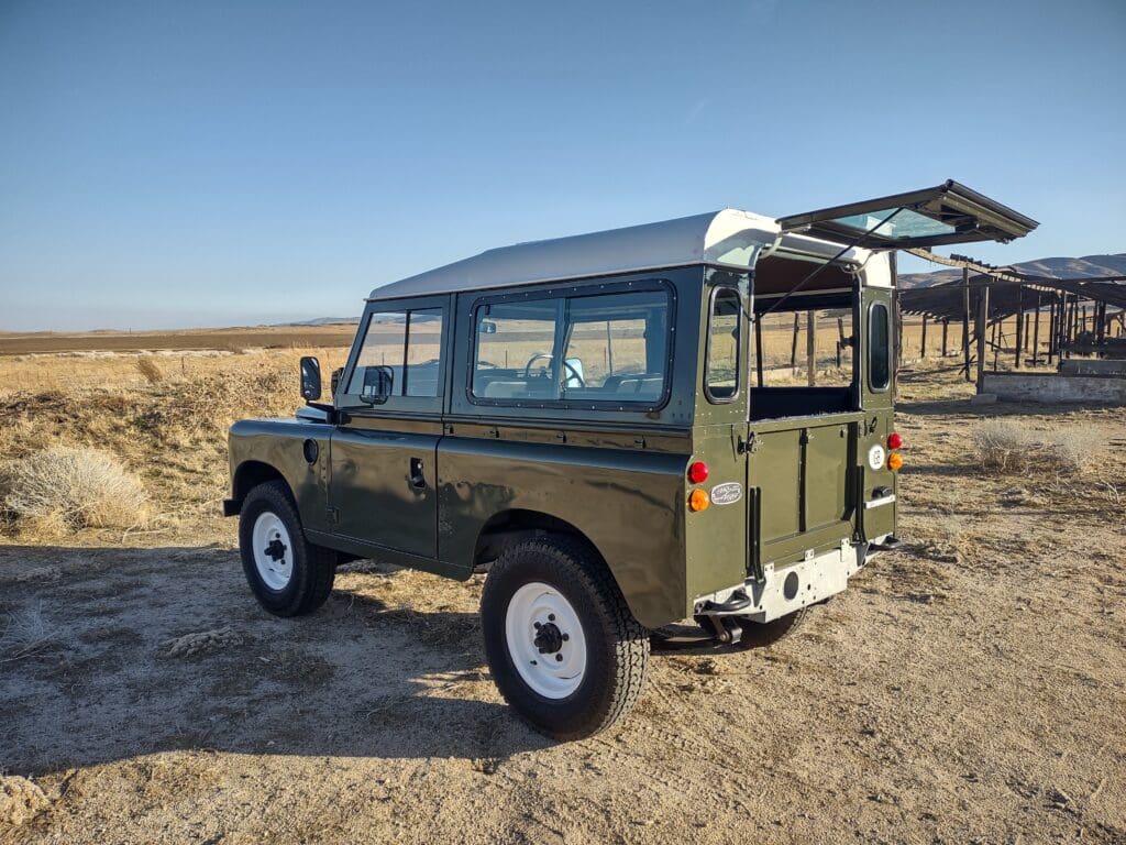 Classic green Land Rover Defender parked in a desert landscape.