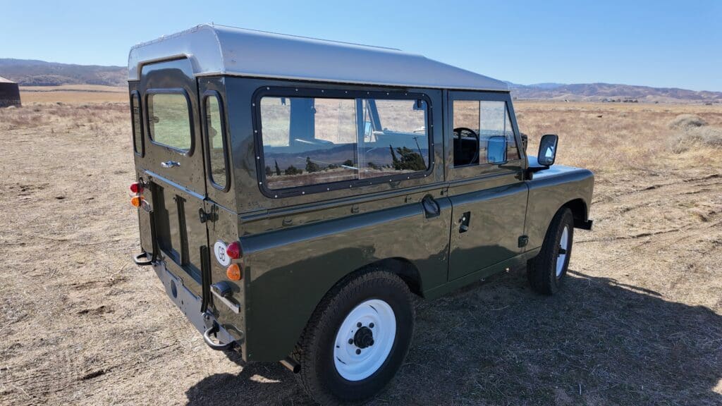 Classic green Land Rover Defender parked in a sunny desert area.