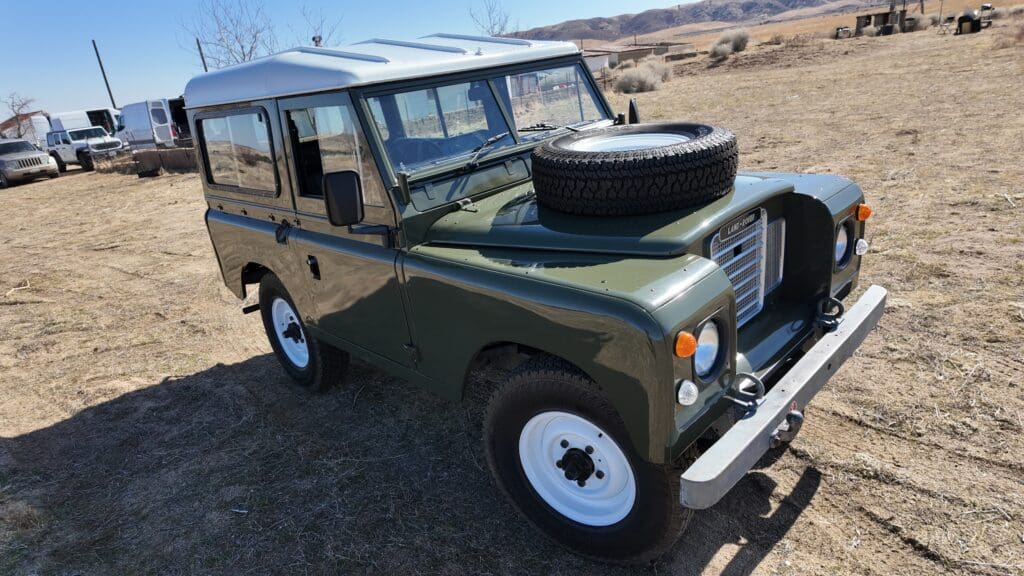 Classic green off-road vehicle with white wheels and a spare tire on the hood.
