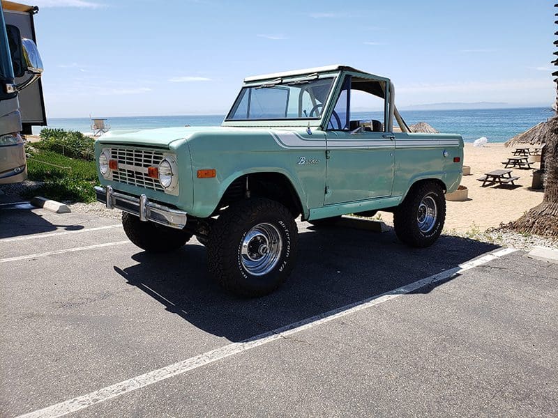 Classic green vintage off-road truck parked near the beach under clear skies.