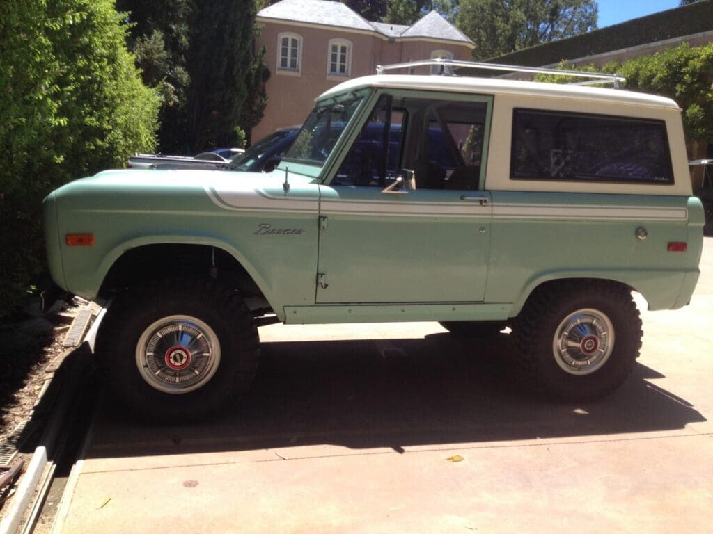 Vintage green and white SUV parked outside a house.