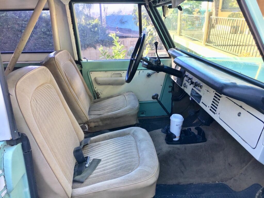Interior of a vintage car with beige seats and manual gear shift.