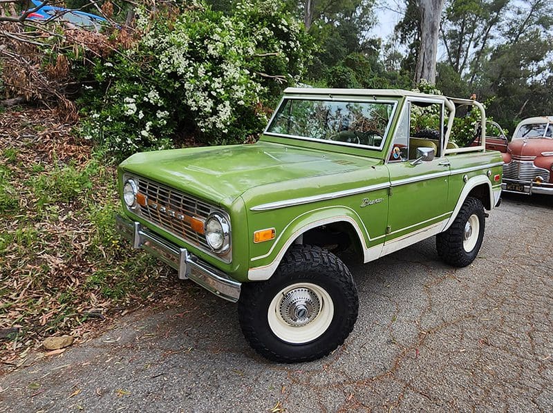 Classic green vintage SUV parked near greenery.