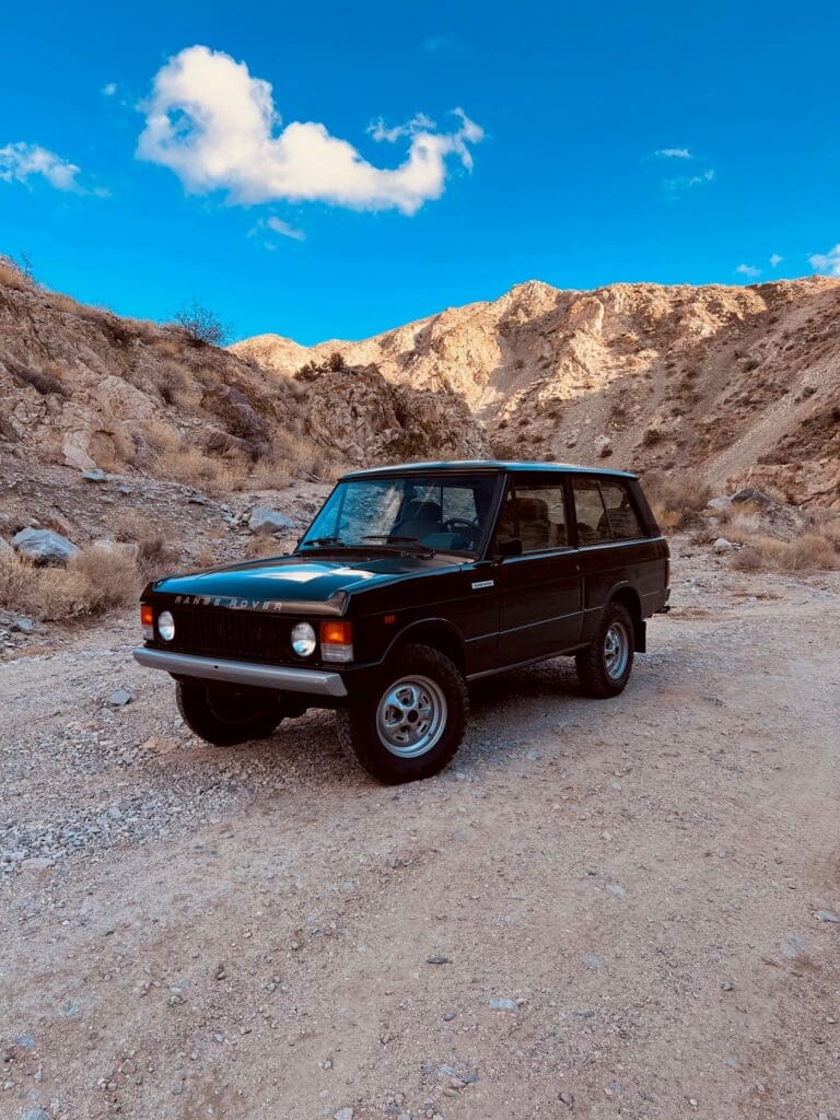 Black SUV parked in a rocky desert landscape under a blue sky.