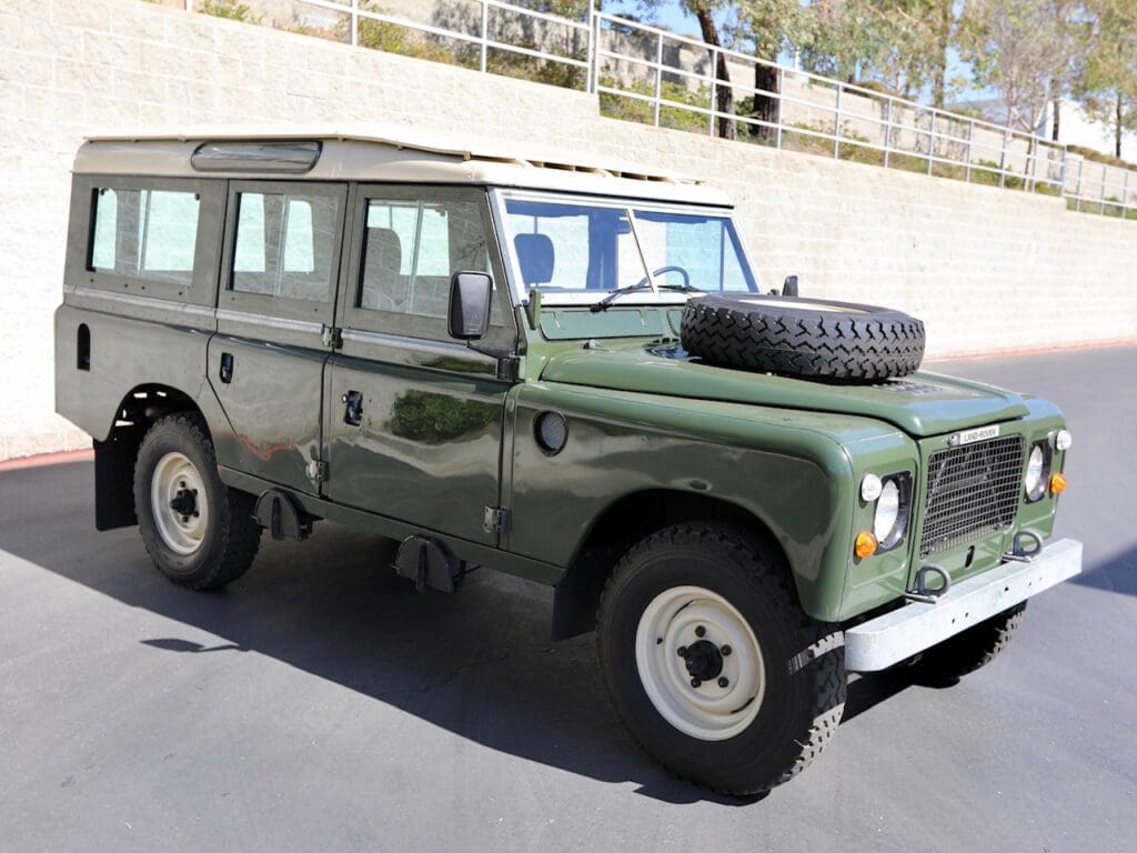 Classic green Land Rover Defender parked outdoors with a spare tire on the hood.