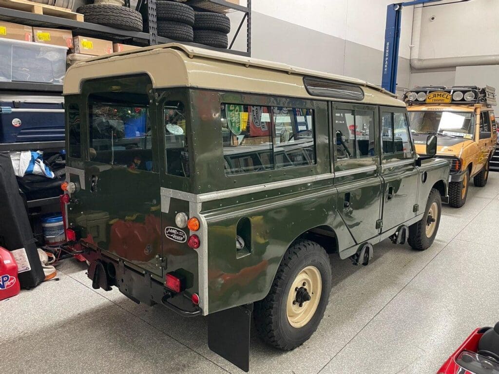 Classic green Land Rover Defender parked indoors with rugged tires and vintage design.