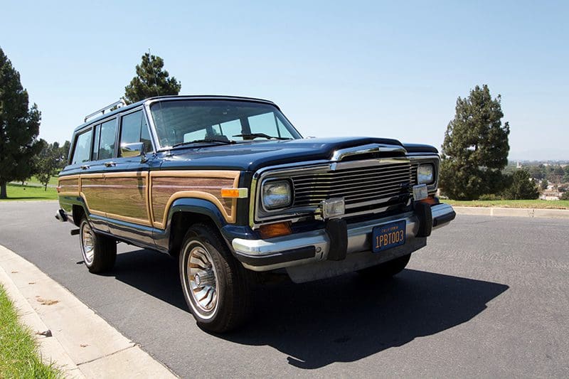 Classic Jeep Wagoneer with wood paneling parked on a sunny street.
