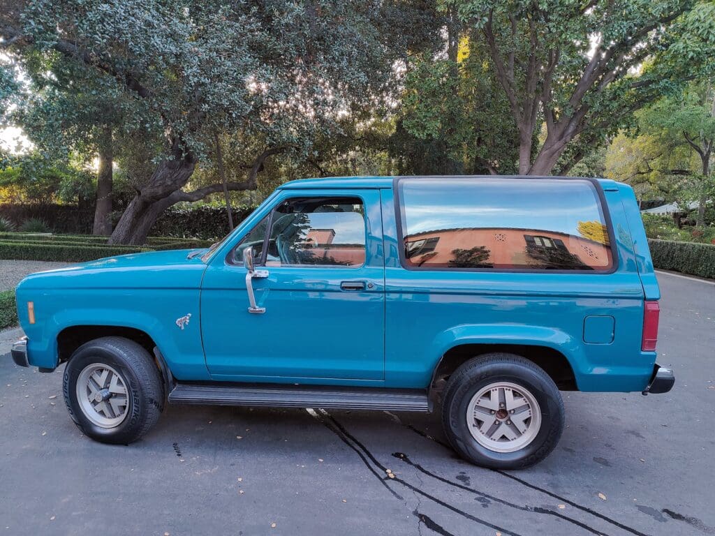 Vintage blue SUV parked outdoors near trees.