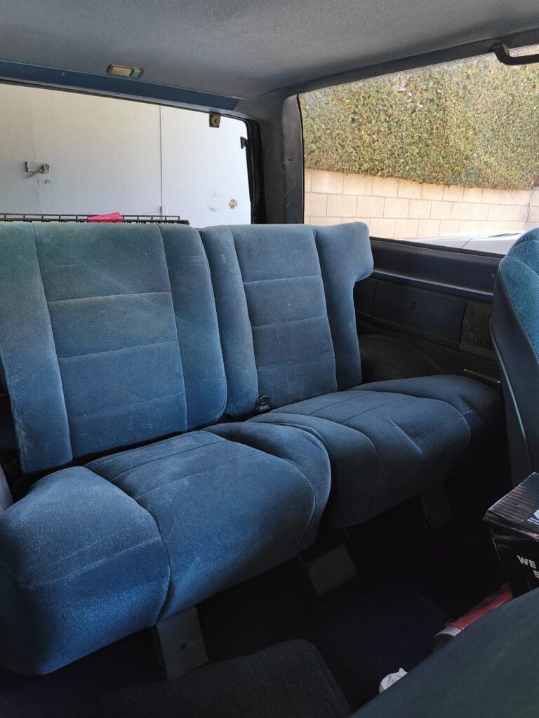Blue fabric car backseat with visible seatbelts and window.