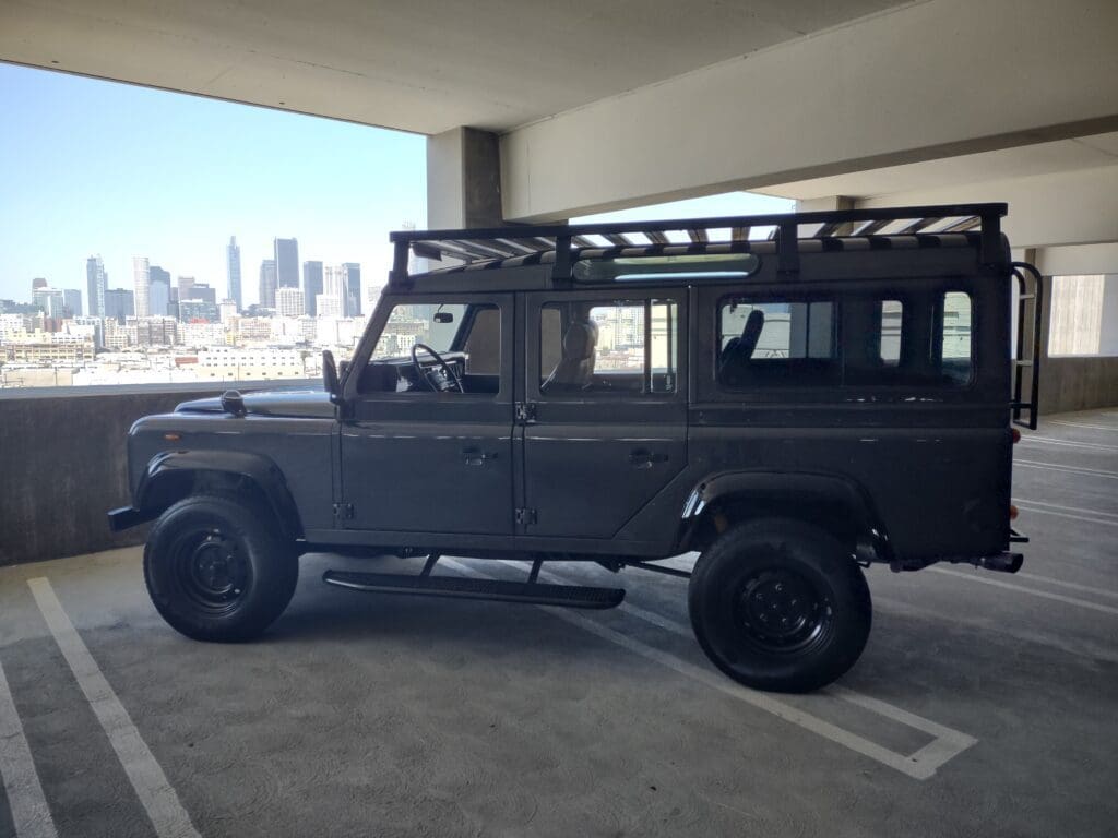 Black Land Rover Defender parked indoors with city skyline in background.