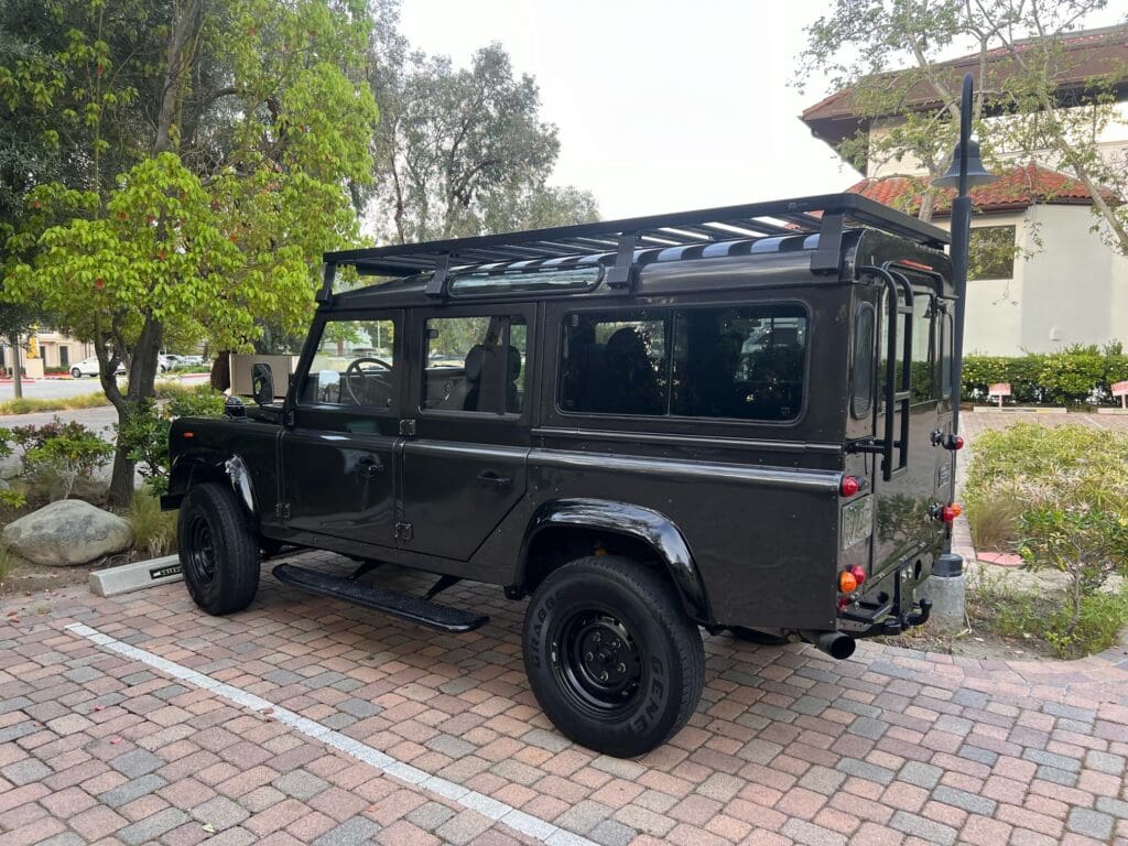 Black off-road vehicle parked on a brick driveway surrounded by greenery.