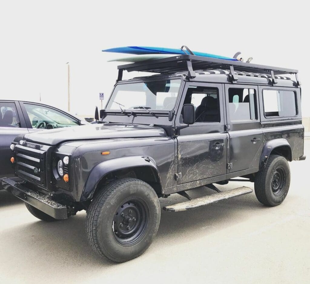 A rugged black off-road SUV with a roof rack and surfboard.