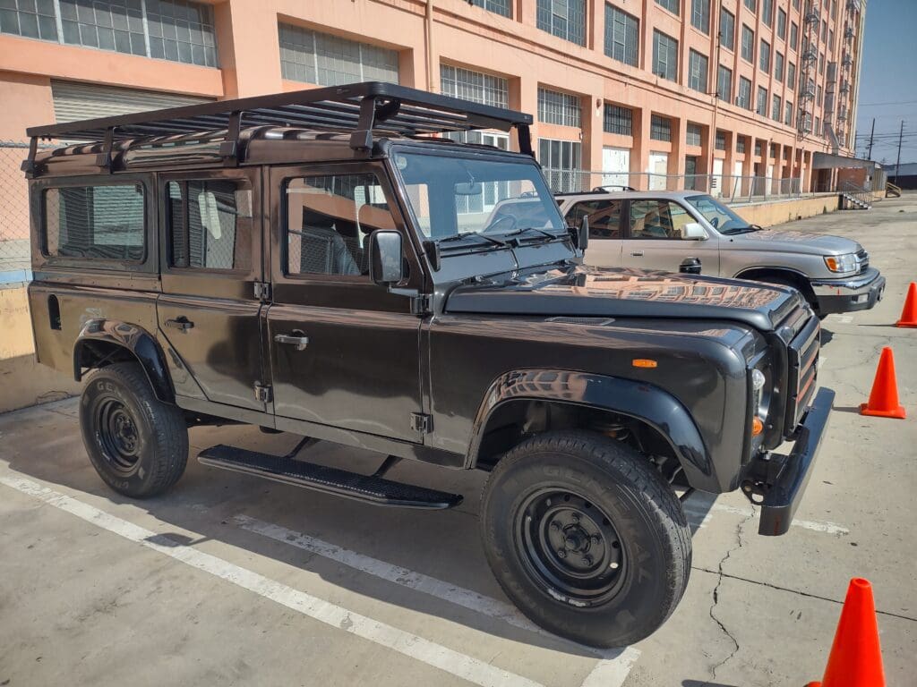 Black Land Rover Defender parked in an outdoor lot near a building.