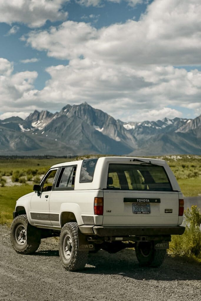White SUV parked in a scenic mountain landscape under a cloudy sky.