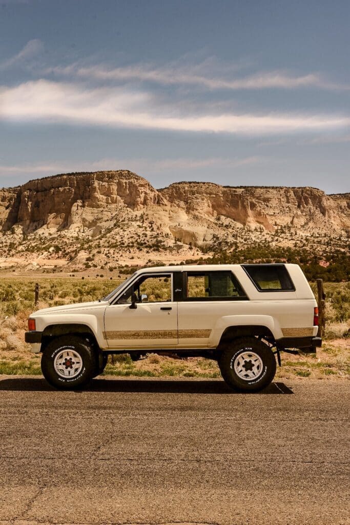 White SUV parked on a desert road with rocky cliffs in the background.