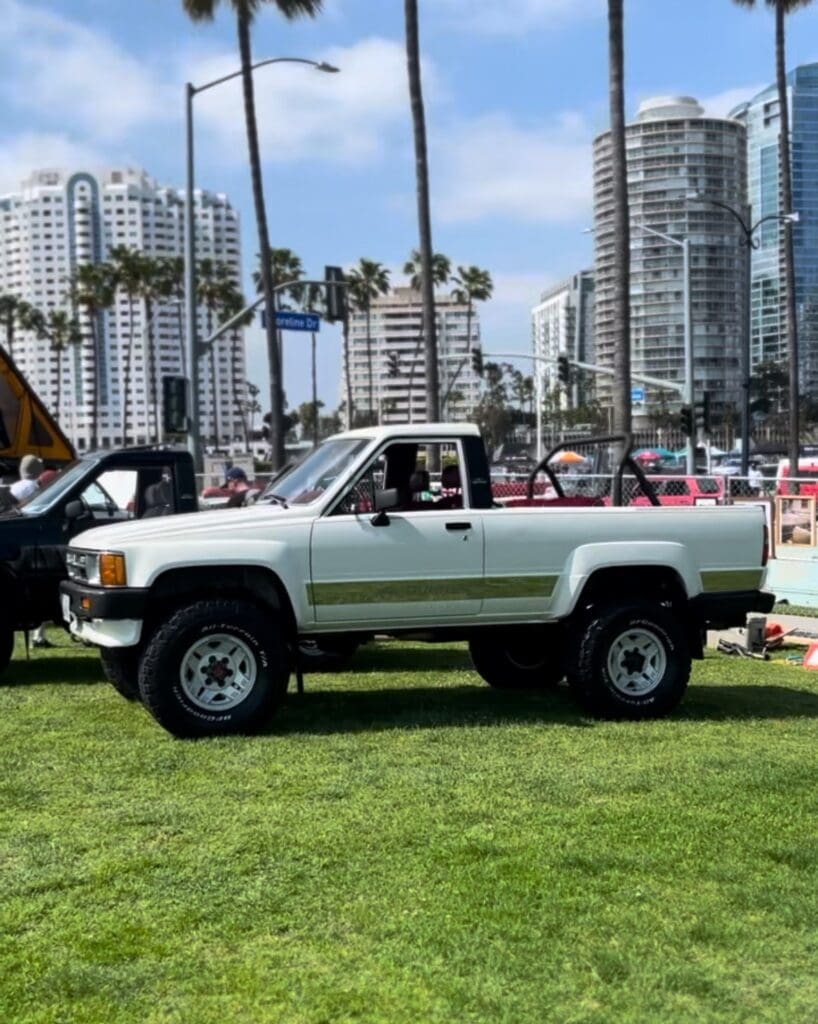 White off-road truck parked on grass in urban area with tall buildings.