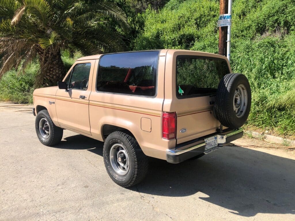 Vintage beige SUV parked on a sunny street with a spare tire mounted on the back.