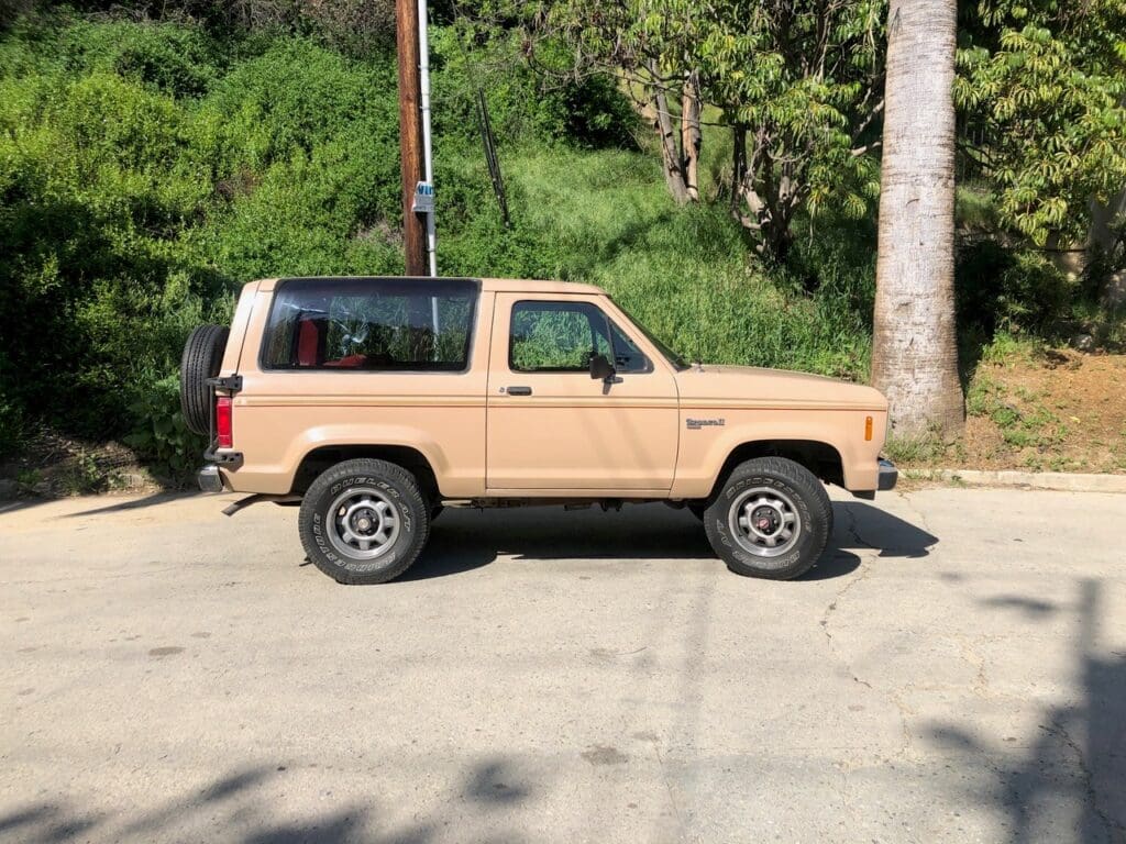 Beige off-road SUV parked on a sunny street with greenery in the background.