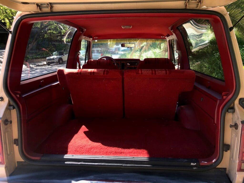 Empty red interior of a vintage car trunk with rear seats visible.