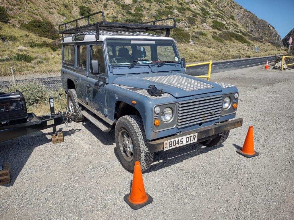 A blue Land Rover Defender parked outdoors with orange cones around.