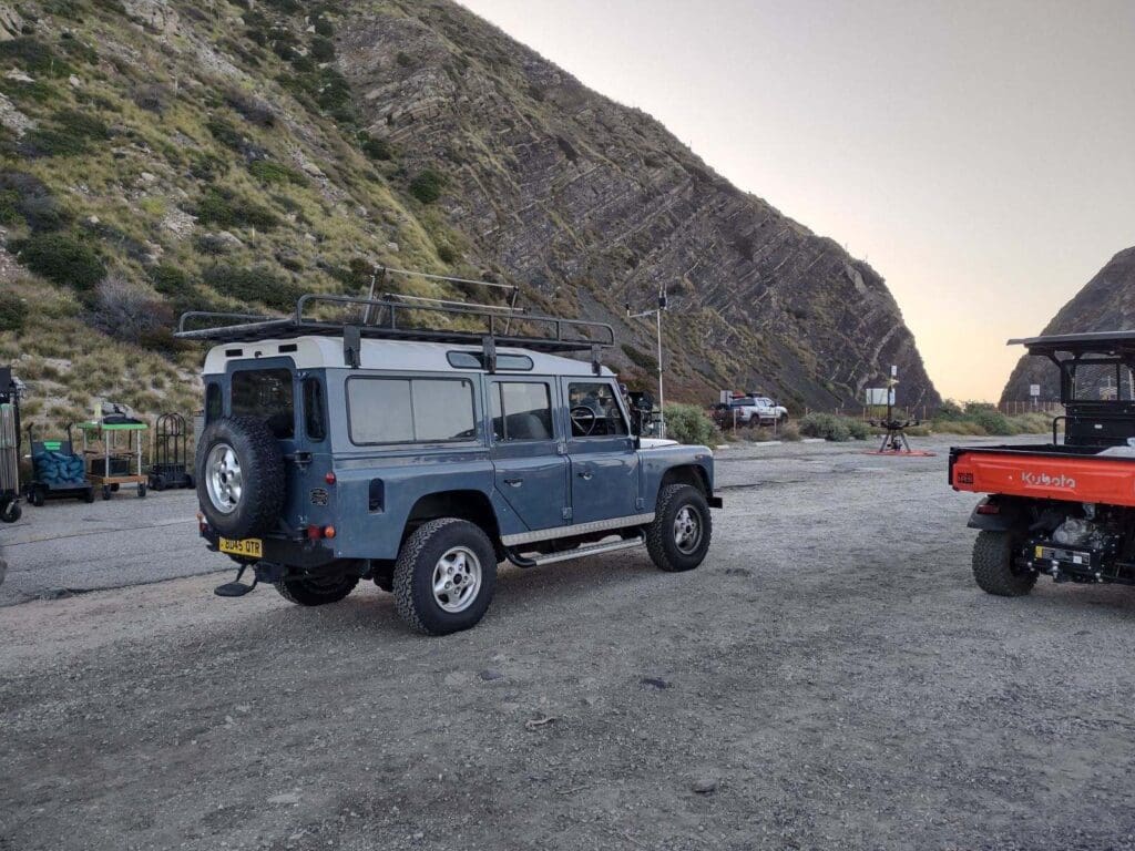 A blue Land Rover Defender parked outdoors with orange cones around.