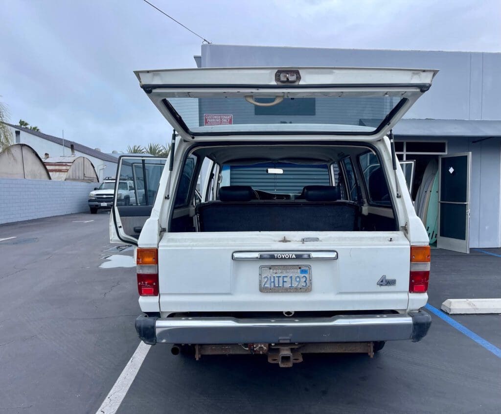 Rear view of a white Toyota Land Cruiser with open hatchback in a parking lot.
