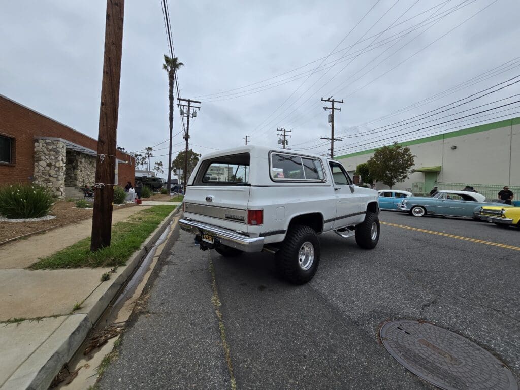 A classic white lifted truck parked on a sunny street.