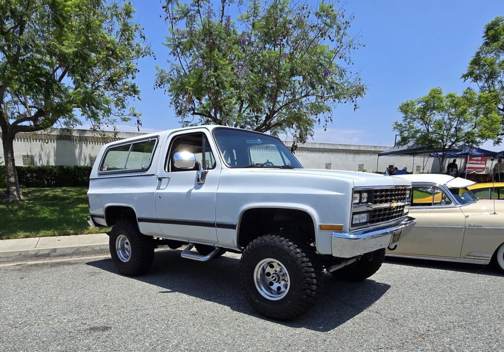 Classic lifted white SUV parked under a tree on a sunny day.